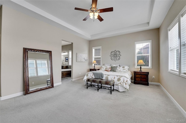bedroom featuring a tray ceiling, carpet floors, multiple windows, and ensuite bath