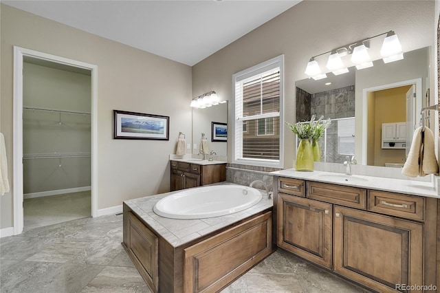 full bath featuring tiled shower, a bath, two vanities, a walk in closet, and baseboards