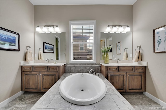 full bath featuring marble look tile flooring, two vanities, a bath, and baseboards