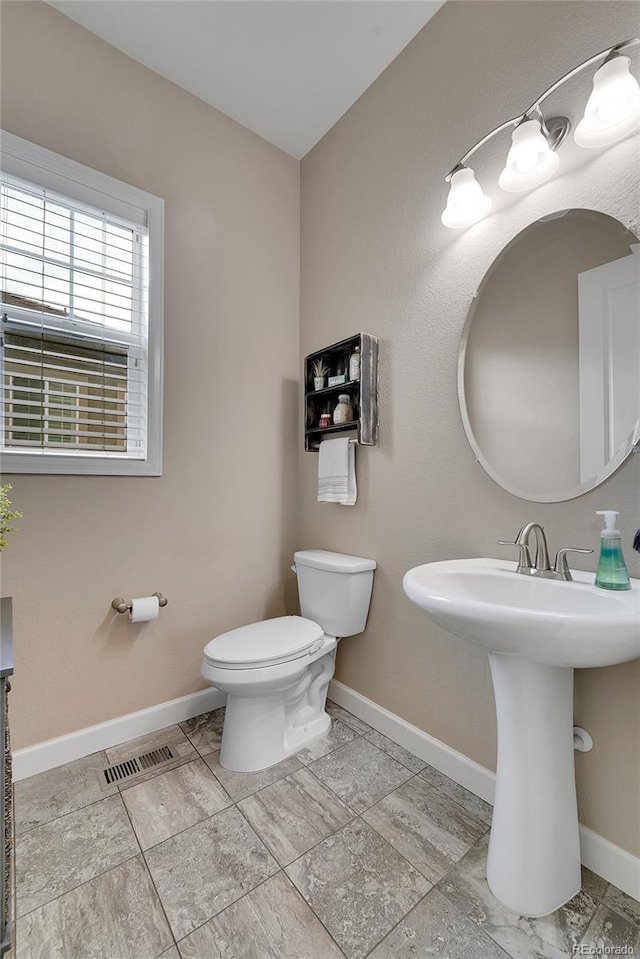 half bathroom featuring baseboards, toilet, and a sink