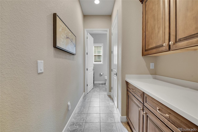 corridor featuring baseboards, a textured wall, and light tile patterned floors