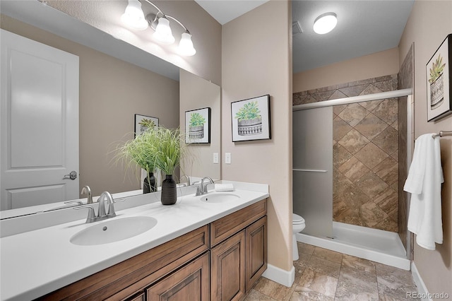bathroom featuring toilet, a shower stall, double vanity, and baseboards