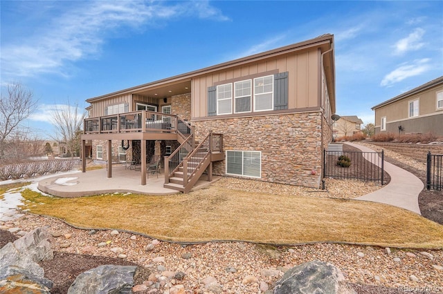 rear view of property featuring stone siding, board and batten siding, a wooden deck, a patio area, and stairs