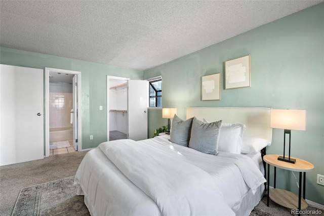 bedroom with a textured ceiling, a spacious closet, ensuite bathroom, a closet, and carpet