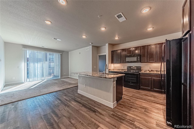 kitchen featuring black appliances, sink, a kitchen island with sink, and hardwood / wood-style flooring