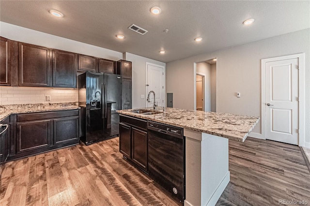 kitchen featuring backsplash, sink, black appliances, a center island with sink, and hardwood / wood-style floors