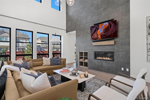 living room with a towering ceiling, wood-type flooring, a tile fireplace, and tile walls