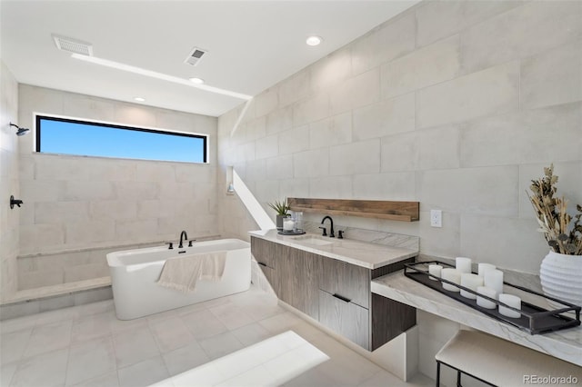 bathroom with tile walls, vanity, a bathtub, and tile patterned flooring