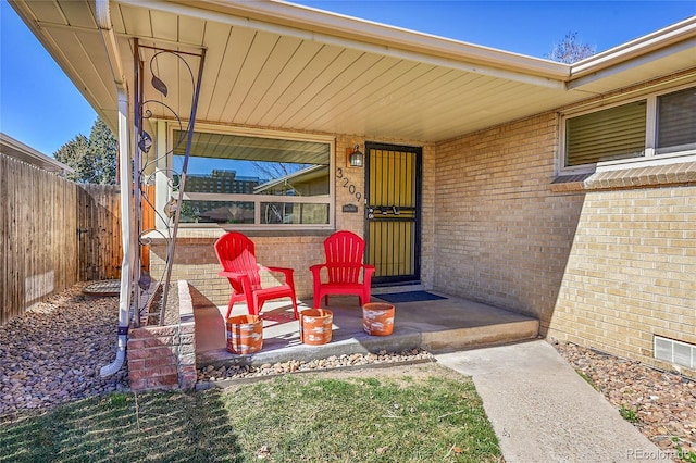 property entrance featuring brick siding, fence, and visible vents