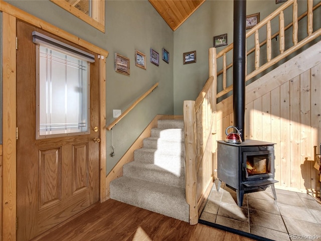 staircase featuring wood-type flooring, a wood stove, and high vaulted ceiling