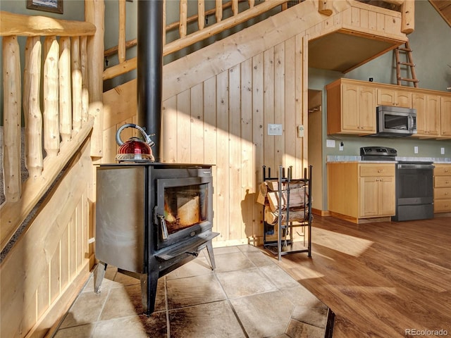 kitchen featuring light brown cabinetry, light wood-type flooring, a wood stove, wooden walls, and stainless steel appliances