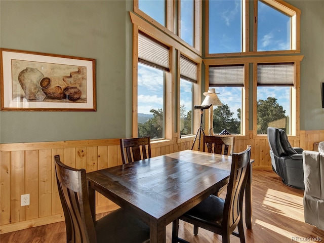 dining area featuring a towering ceiling, wooden walls, and light hardwood / wood-style floors