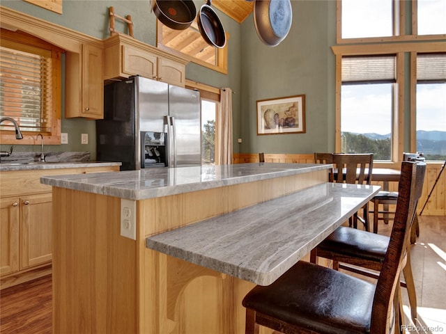 kitchen featuring sink, stainless steel fridge, a kitchen breakfast bar, a center island, and light brown cabinets