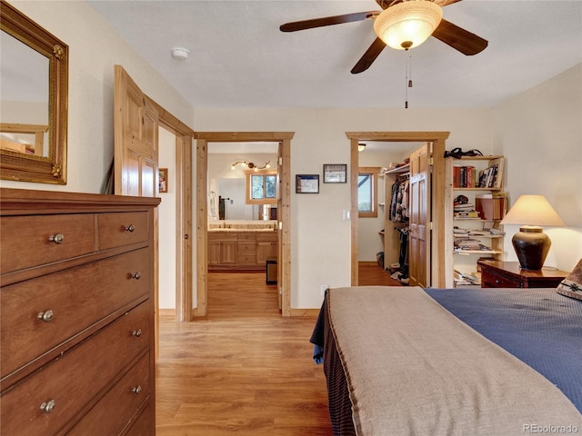 bedroom featuring ensuite bathroom, a walk in closet, ceiling fan, light wood-type flooring, and a closet