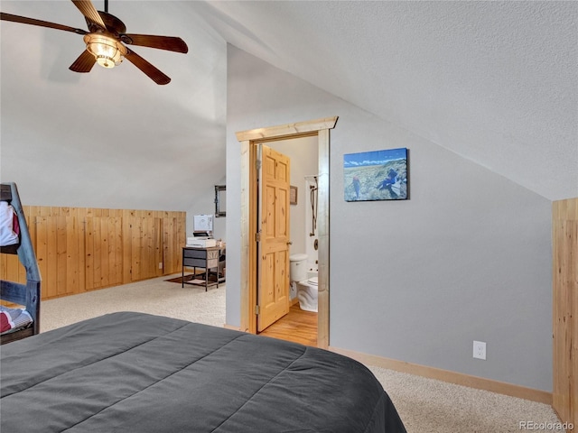 carpeted bedroom with ceiling fan, connected bathroom, a textured ceiling, vaulted ceiling, and wood walls