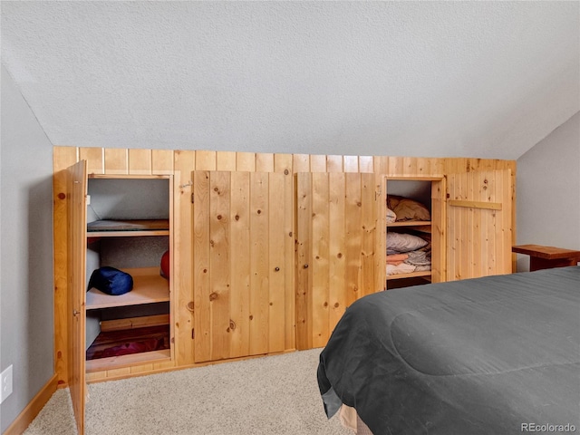 carpeted bedroom with lofted ceiling, a textured ceiling, and wood walls