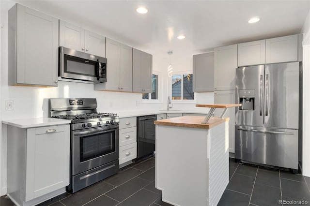 kitchen featuring butcher block countertops, stainless steel appliances, a center island, decorative light fixtures, and sink