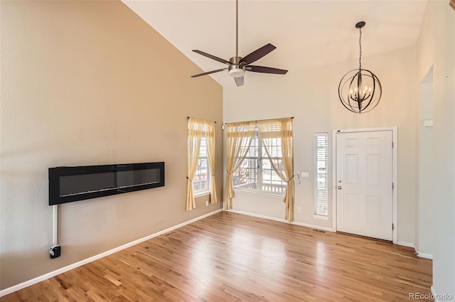 foyer with high vaulted ceiling, ceiling fan with notable chandelier, baseboards, and wood finished floors