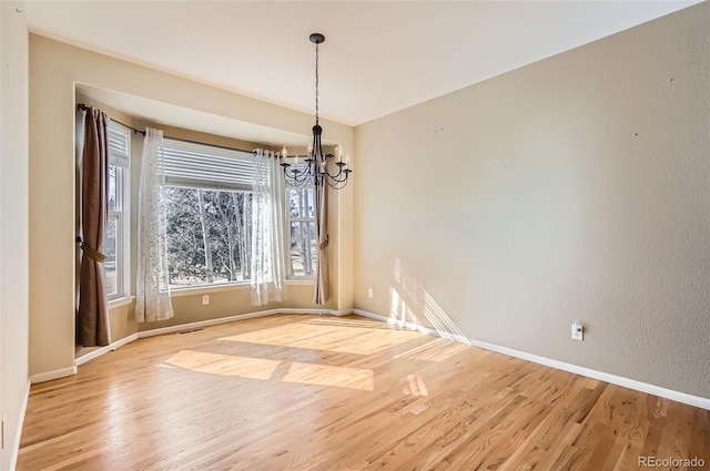 unfurnished dining area featuring light wood-type flooring, visible vents, baseboards, and an inviting chandelier