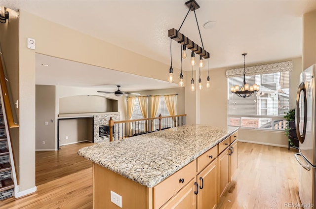 kitchen with light wood finished floors, a tile fireplace, light stone counters, freestanding refrigerator, and light brown cabinetry