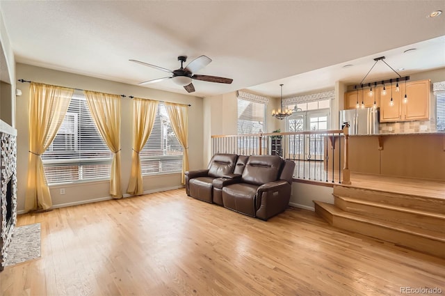 living area with light wood-type flooring, baseboards, and ceiling fan with notable chandelier