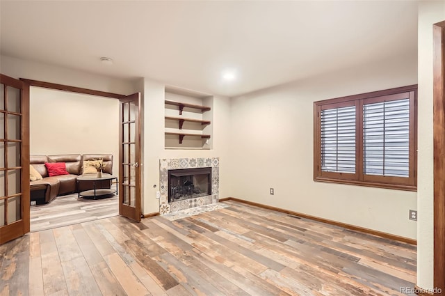 living area with a tiled fireplace, baseboards, wood finished floors, and french doors