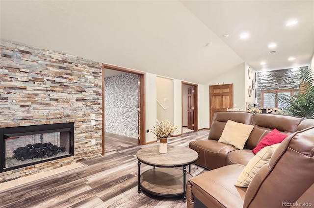 living area featuring lofted ceiling, light wood finished floors, and a stone fireplace