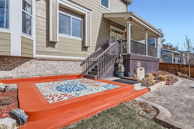 doorway to property featuring a patio, brick siding, and fence