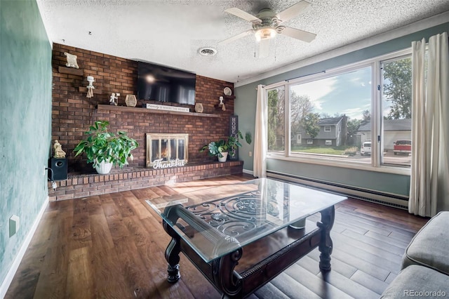 living room featuring wood-type flooring, ceiling fan, a fireplace, and a textured ceiling