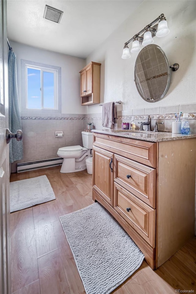 bathroom featuring tile walls, a baseboard radiator, hardwood / wood-style floors, vanity, and toilet