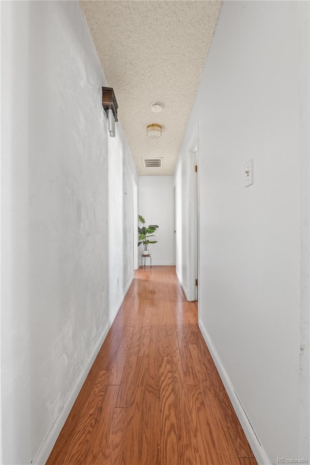 hallway featuring visible vents, a textured ceiling, baseboards, and wood finished floors