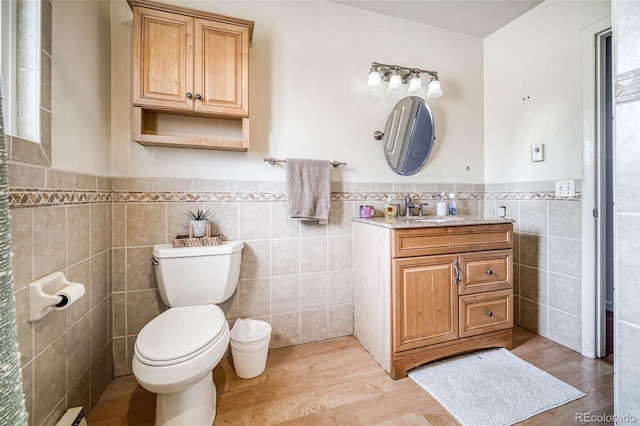 bathroom with wainscoting, toilet, wood finished floors, vanity, and tile walls