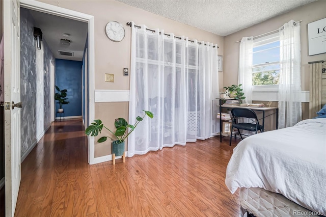 bedroom featuring visible vents, a textured ceiling, baseboards, and wood finished floors