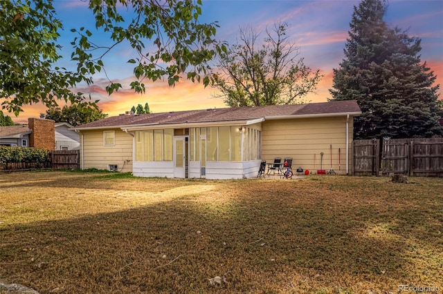 back of house at dusk featuring a lawn, fence, and a sunroom