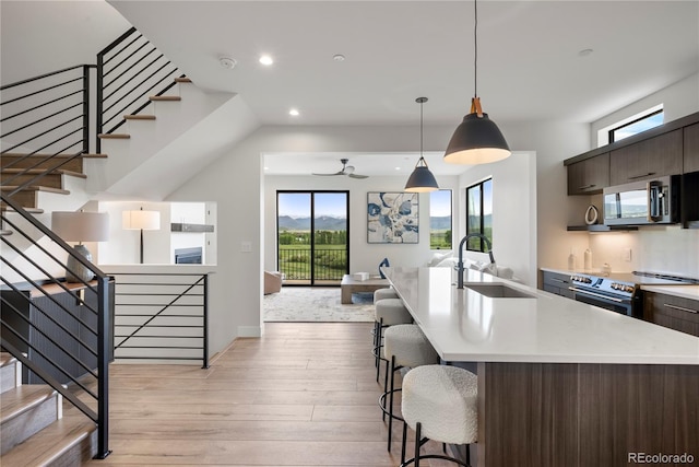 kitchen featuring dark brown cabinetry, sink, light hardwood / wood-style flooring, a center island with sink, and appliances with stainless steel finishes