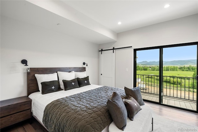 bedroom with a mountain view, a barn door, access to exterior, and wood-type flooring