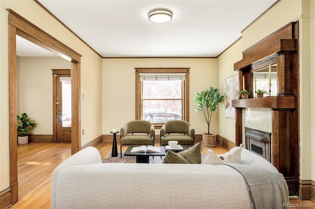 living room with light wood-type flooring, baseboards, a fireplace, and ornamental molding