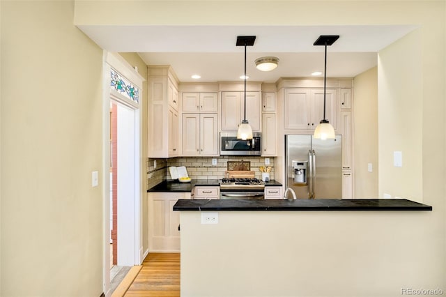 kitchen featuring tasteful backsplash, dark countertops, light wood-style flooring, appliances with stainless steel finishes, and a peninsula