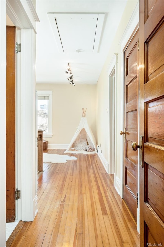 corridor with baseboards, attic access, and light wood-style floors