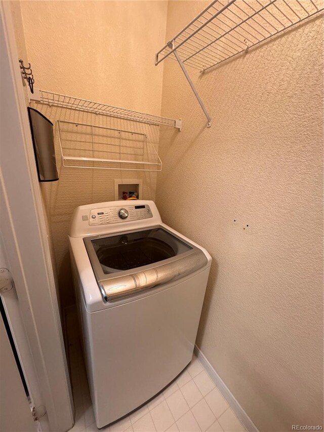 clothes washing area with a textured wall, washer / dryer, and light tile patterned floors
