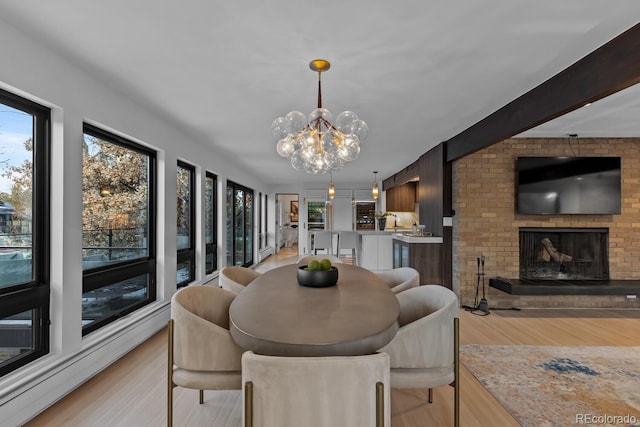 dining area with beam ceiling, a brick fireplace, light wood-type flooring, and an inviting chandelier