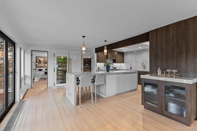 kitchen with a baseboard radiator, decorative backsplash, dark brown cabinetry, light wood-style floors, and modern cabinets