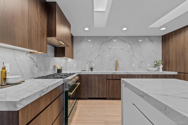 kitchen with tasteful backsplash, light stone countertops, a skylight, high end range, and modern cabinets