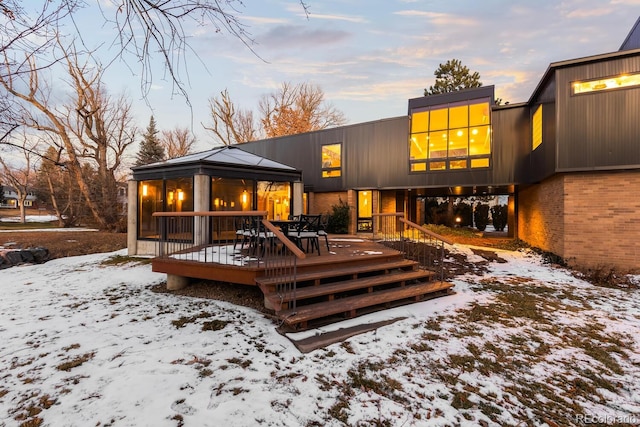 snow covered property with a gazebo, a wooden deck, and brick siding