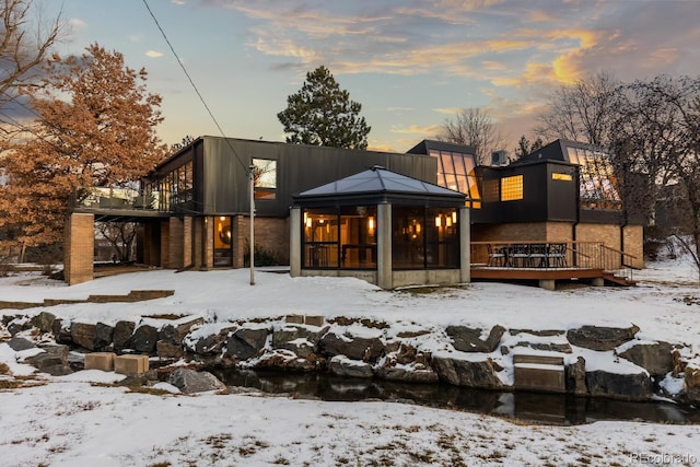 snow covered property featuring a carport, a deck, and a sunroom