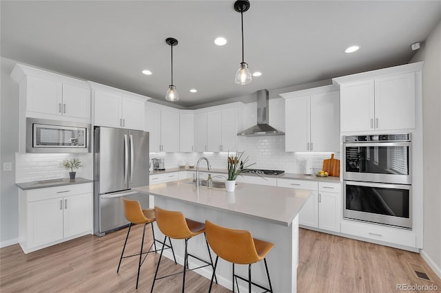 8839 Culebra St, Arvada, CO 80007 - kitchen with stainless steel appliances, wall chimney range hood, decorative backsplash, recessed lighting, and light wood-type flooring