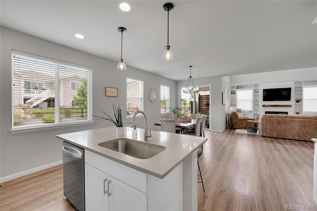 8839 Culebra St, Arvada, CO 80007 - kitchen featuring stainless steel dishwasher, light countertops, light wood-style floors, white cabinets, and decorative light fixtures