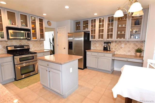 kitchen with tasteful backsplash, gray cabinetry, stainless steel appliances, a kitchen island, and hanging light fixtures