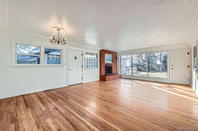 unfurnished living room featuring a chandelier, wood-type flooring, a textured ceiling, and a brick fireplace