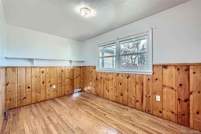 bonus room with a textured ceiling, light hardwood / wood-style floors, and wooden walls